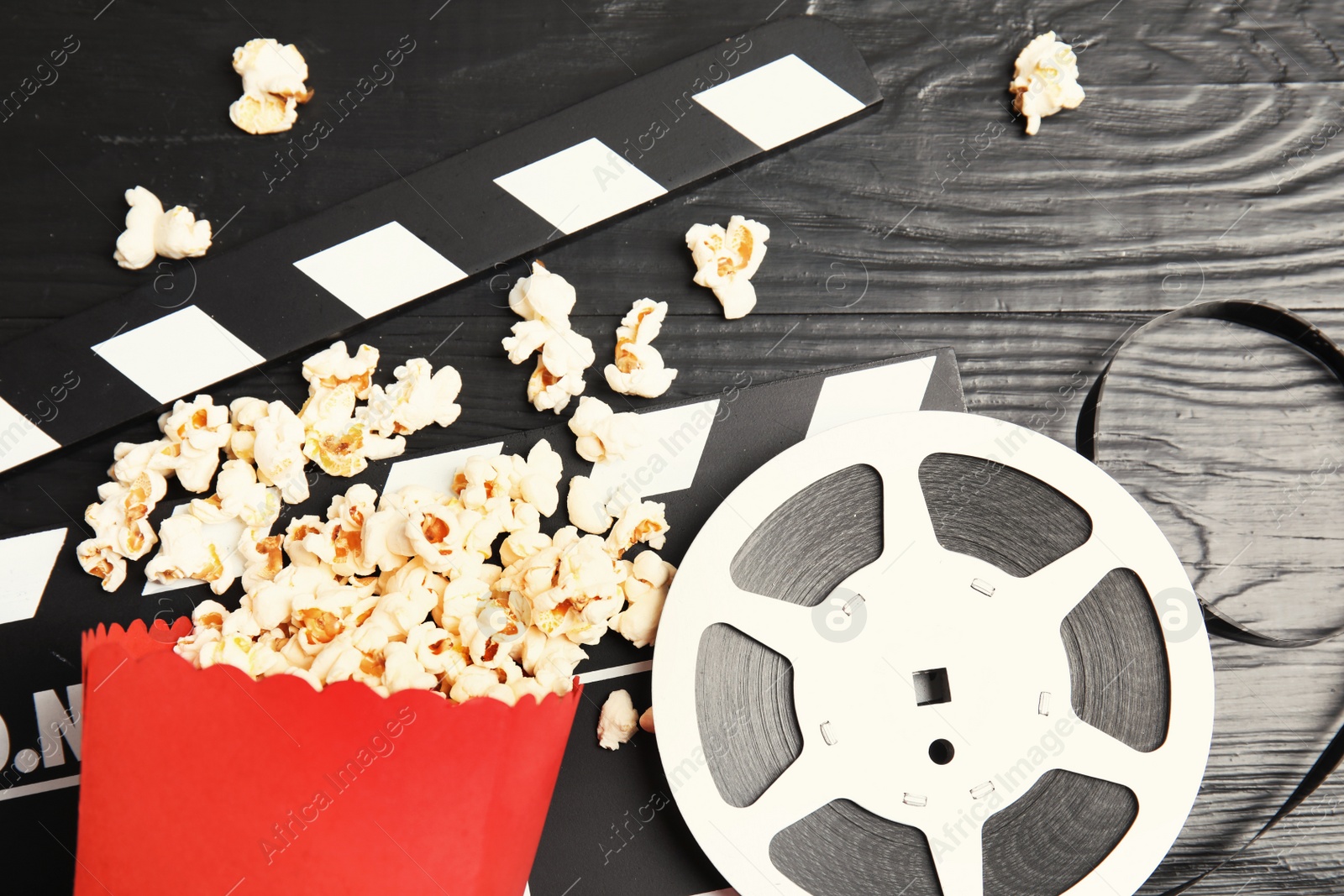 Photo of Tasty popcorn, film reel and clapperboard on wooden background, top view. Cinema snack