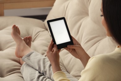 Photo of Young woman using e-book reader on sofa at home, closeup