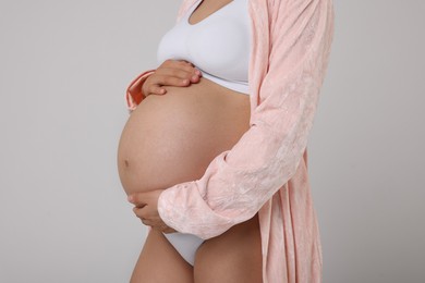 Pregnant woman in stylish comfortable underwear and robe on grey background, closeup