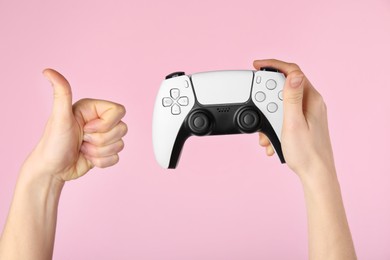 Woman with game controller showing thumbs up on pink background, closeup