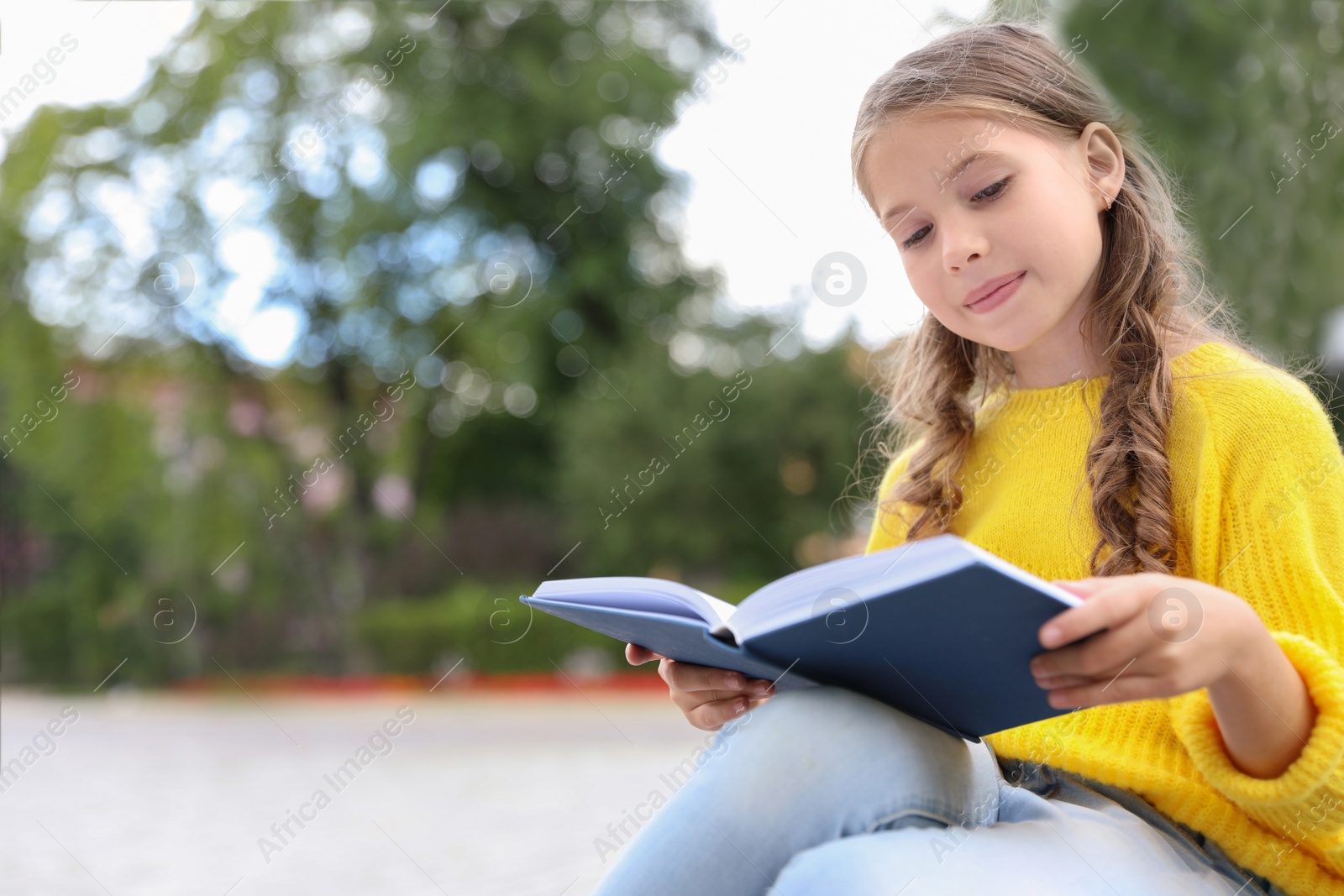 Photo of Cute little girl reading book in green park