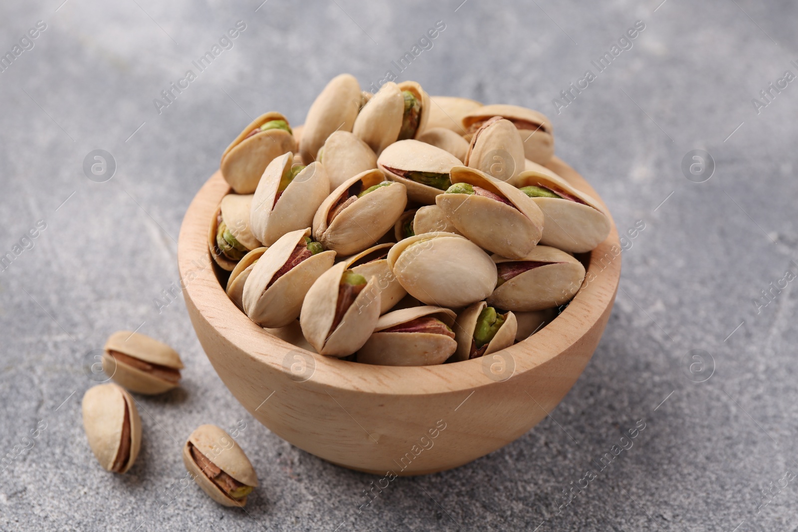 Photo of Delicious pistachios in bowl on grey textured table