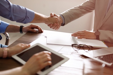 Photo of Business partners shaking hands at table after meeting in office, closeup