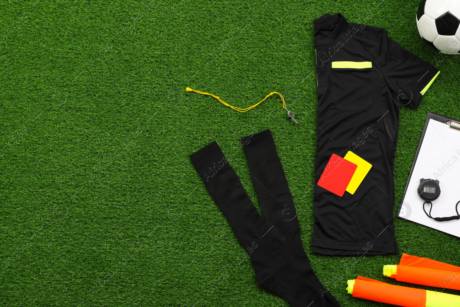 Photo of Uniform, soccer ball and other referee equipment on green grass, flat lay. Space for text