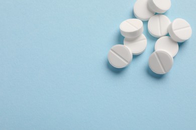 Photo of Pile of white pills on light blue background, above view. Space for text