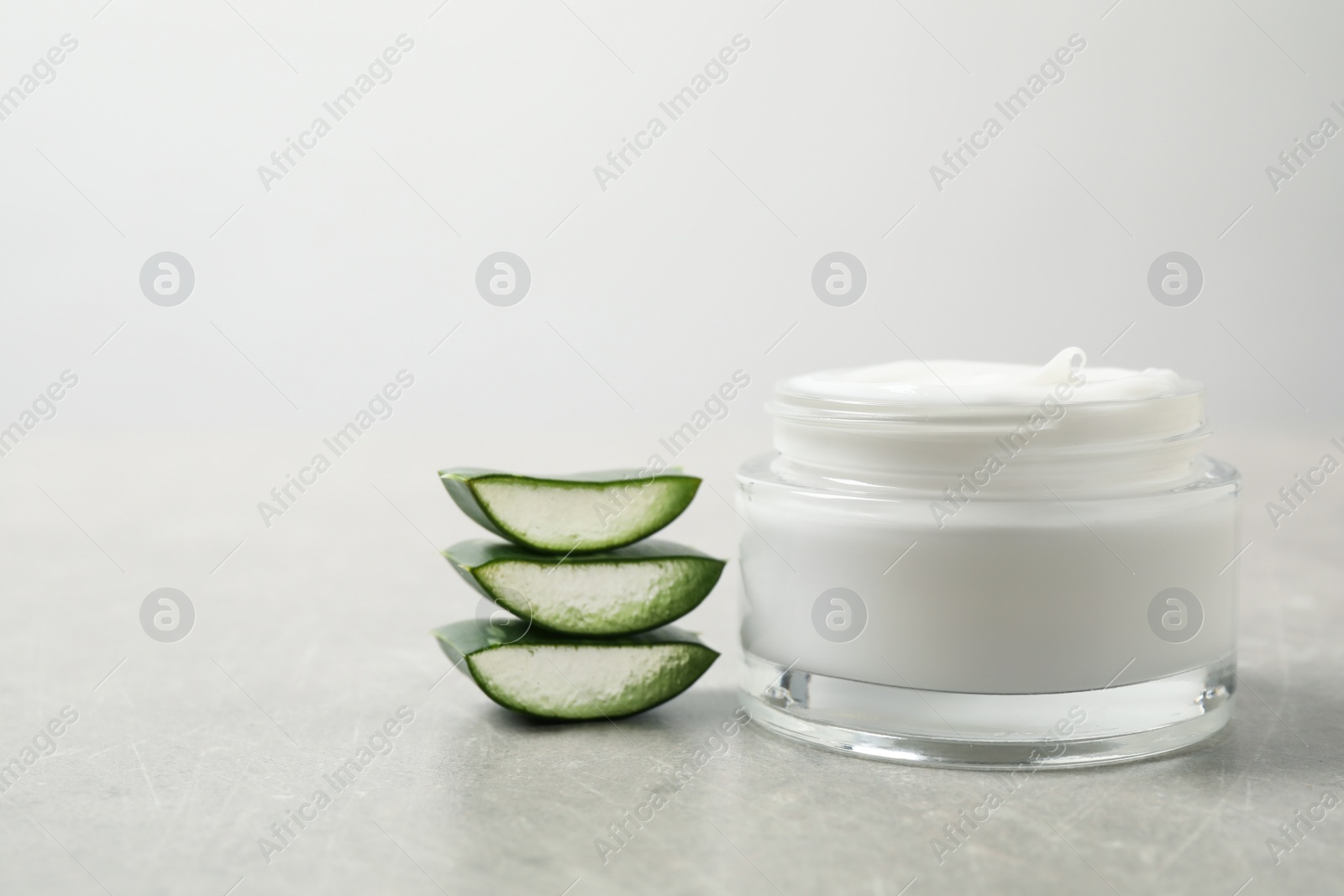 Photo of Open jar of cream and cut aloe on grey table. Organic cosmetics