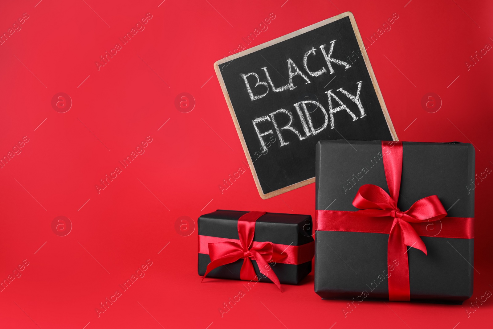Photo of Gift boxes and chalkboard with words Black Friday on red background, space for text