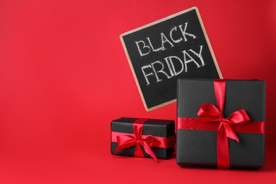 Photo of Gift boxes and chalkboard with words Black Friday on red background, space for text