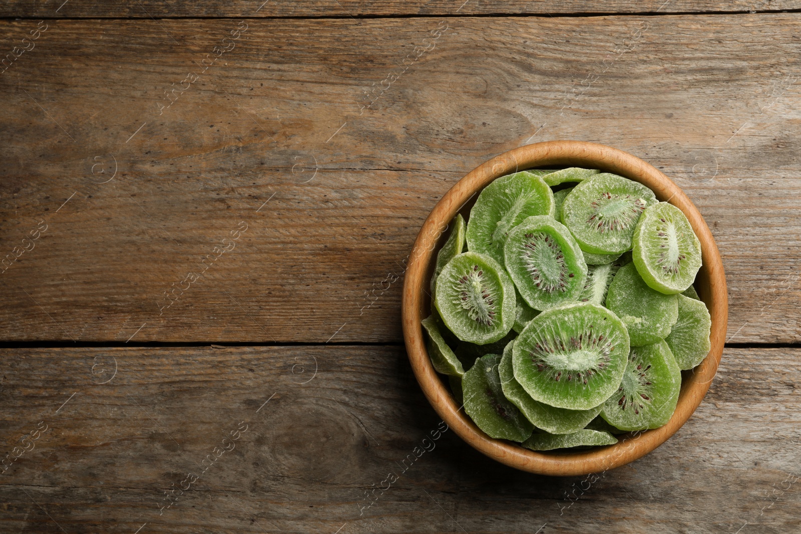 Photo of Bowl of dried kiwi on wooden background, top view with space for text. Tasty and healthy fruit