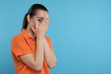 Photo of Embarrassed woman covering face on light blue background. Space for text