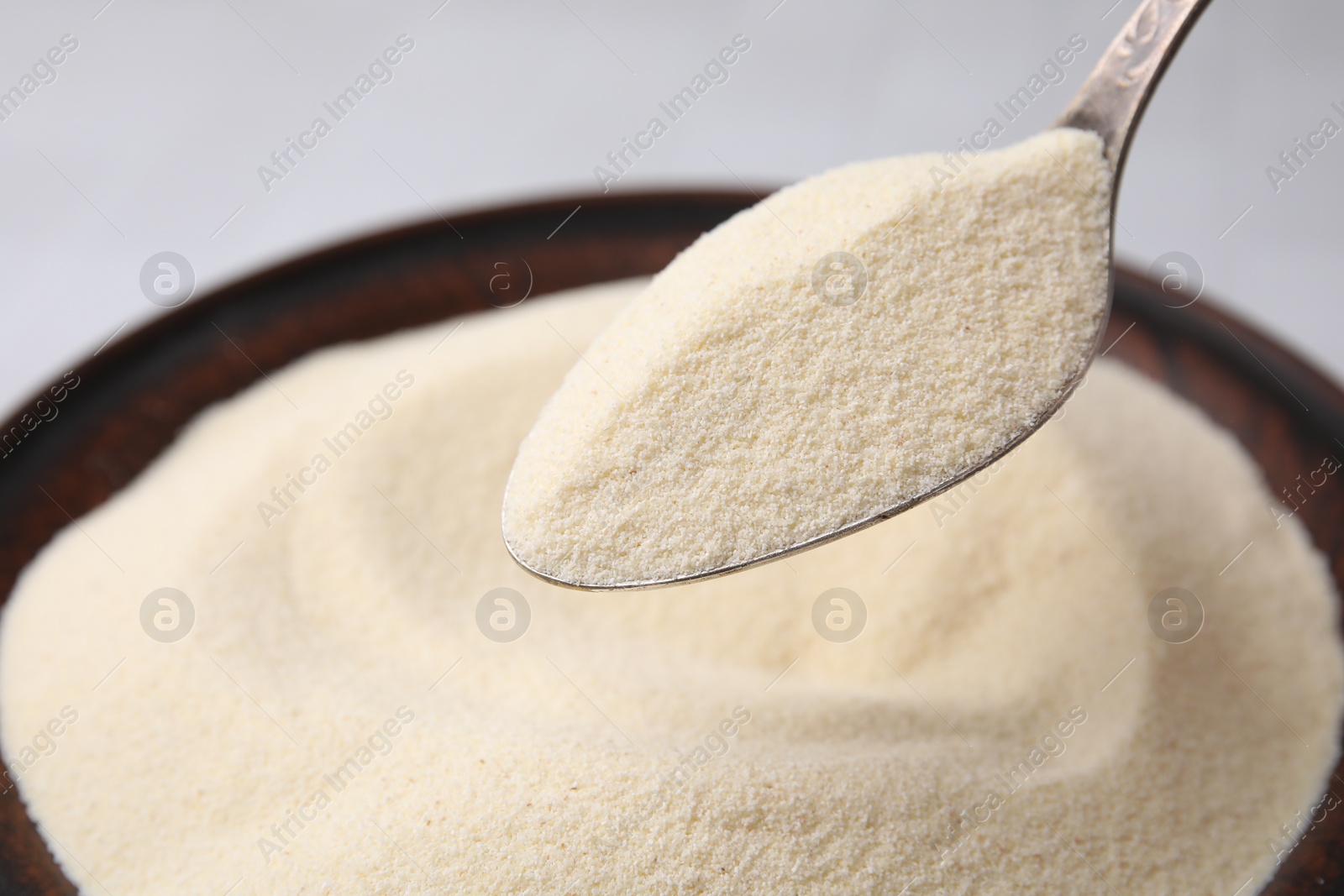 Photo of Uncooked organic semolina in spoon over bowl, closeup