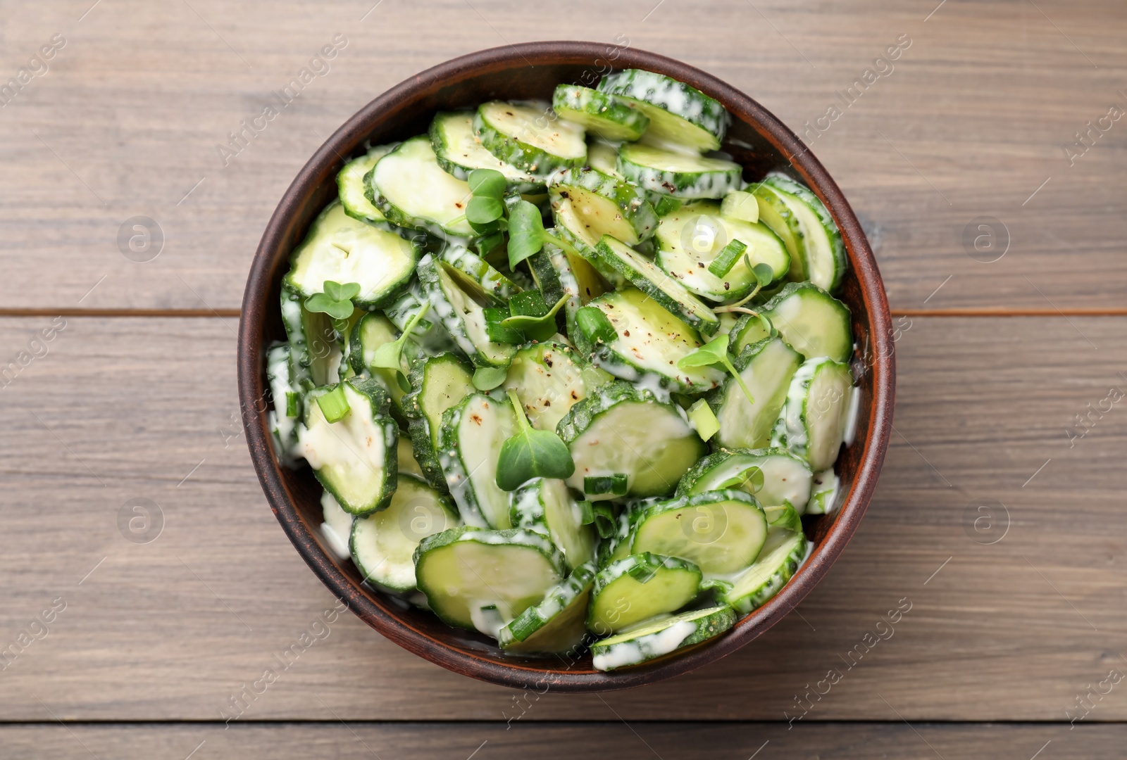 Photo of Bowl of delicious cucumber salad on wooden table, top view