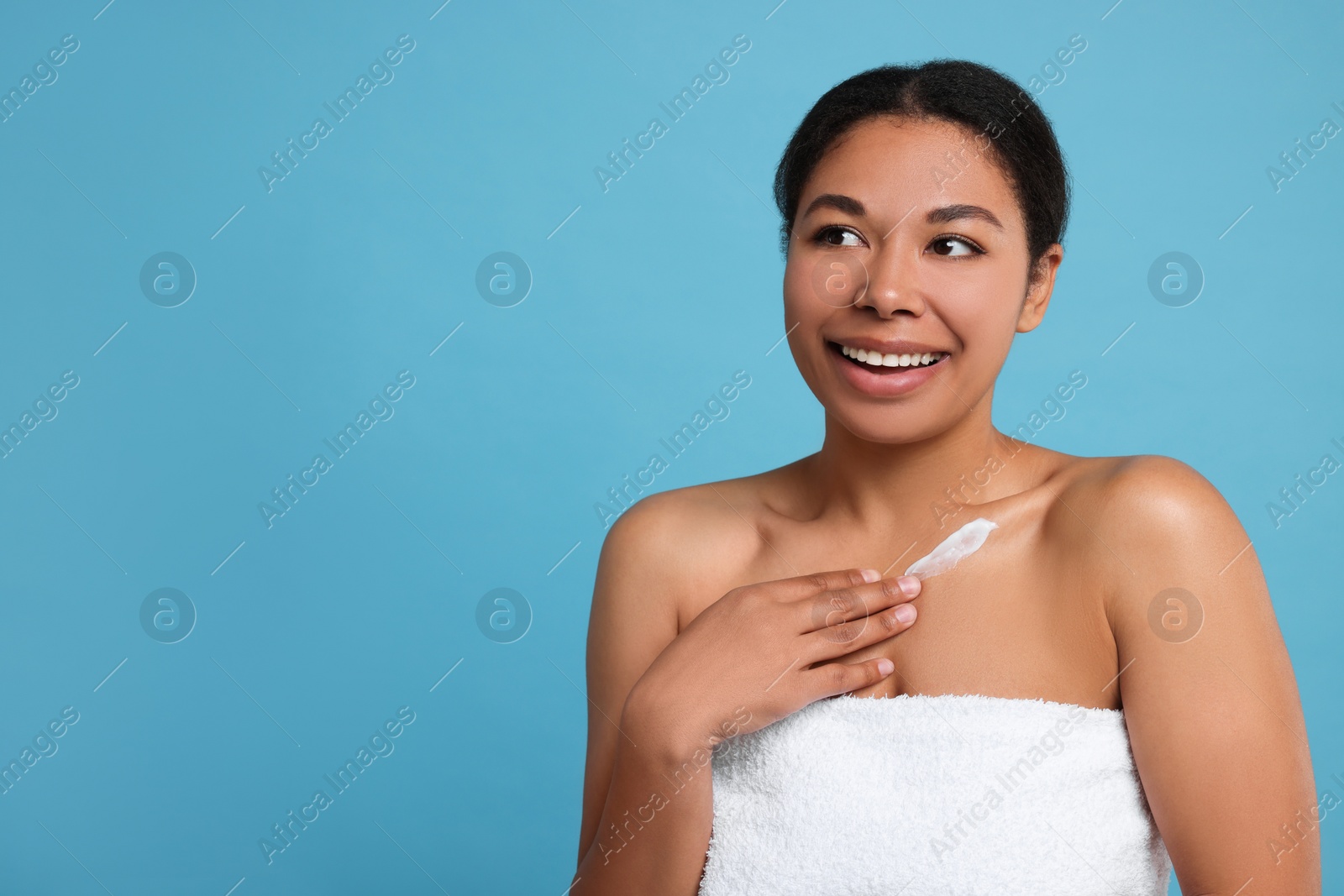 Photo of Young woman applying cream onto body on light blue background. Space for text