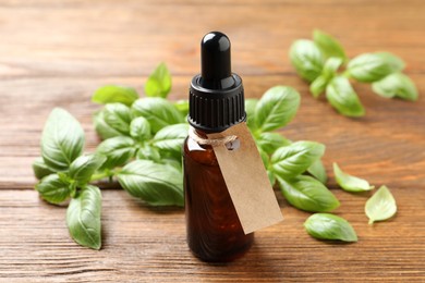 Photo of Glass bottle of basil essential oil and leaves on wooden table