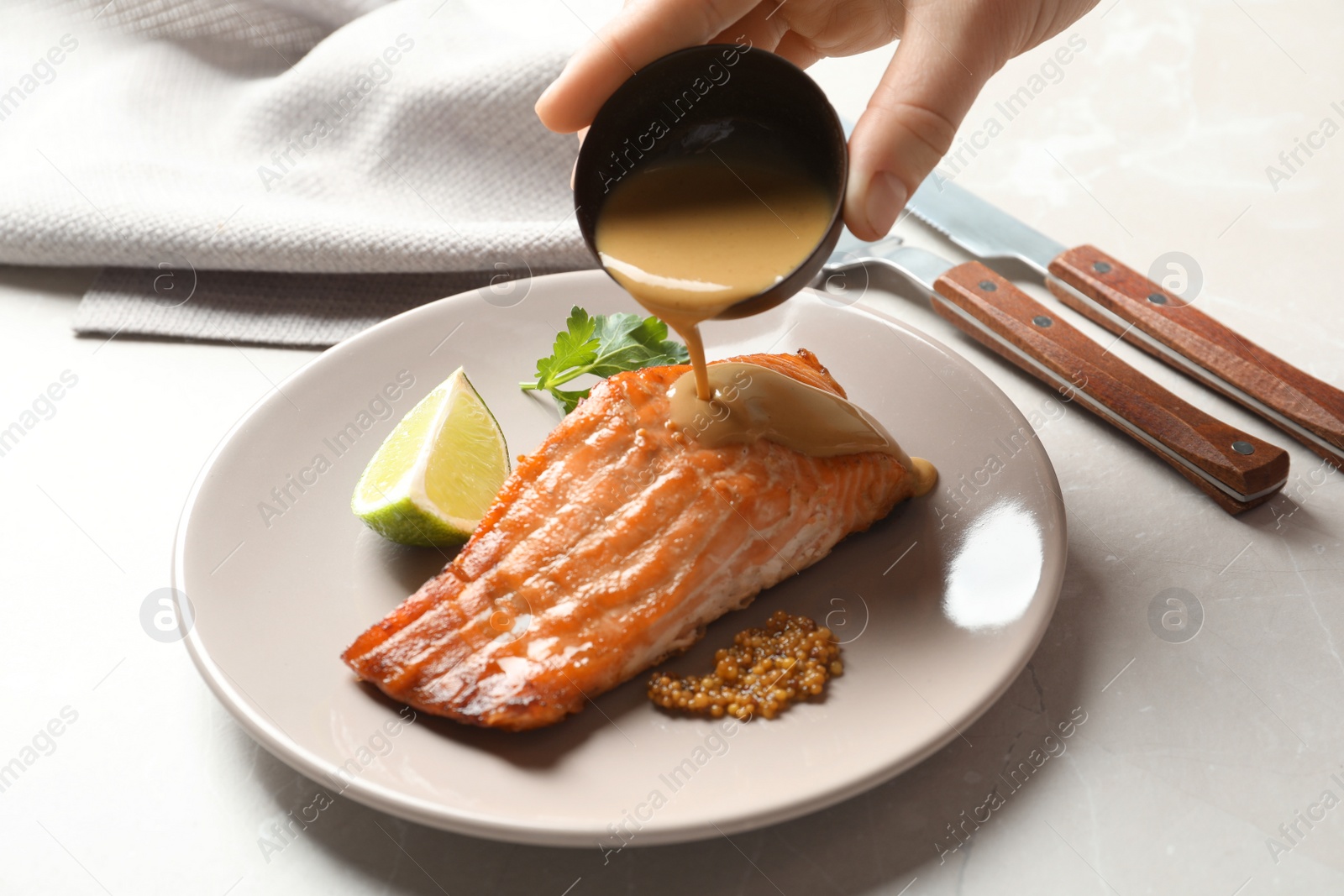 Photo of Woman pouring sauce onto tasty cooked salmon on plate, closeup