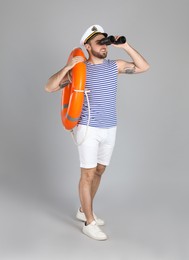 Sailor with binoculars and ring buoy on light grey background