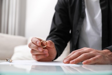 Man with wedding ring and divorce papers at table indoors, closeup. Space for text