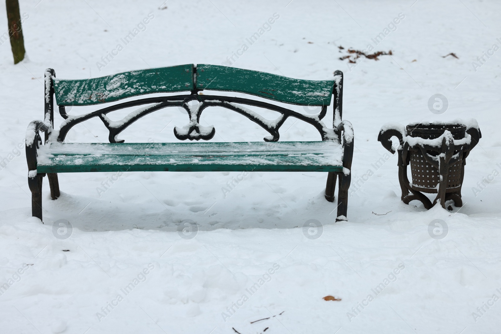 Photo of Green wooden bench and garbage bin covered in snow outdoors