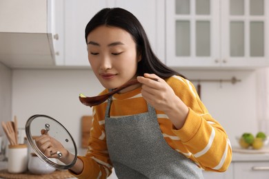 Photo of Beautiful woman cooking and tasting soup in kitchen