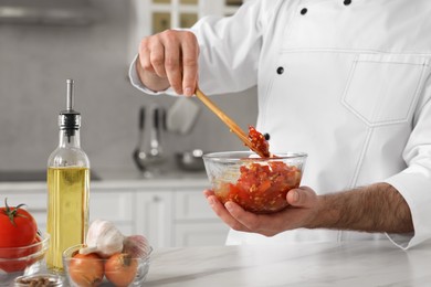 Professional chef making delicious tomato sauce at white marble table indoors, closeup