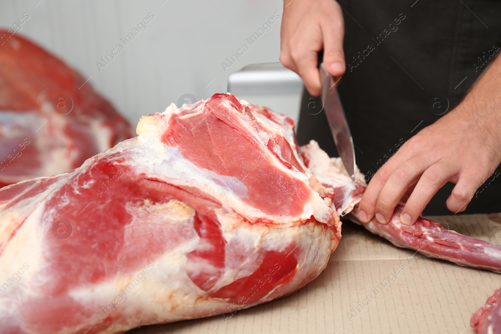 Photo of Butcher cutting fresh raw meat on counter in shop, closeup