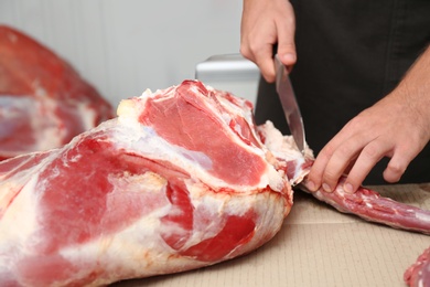 Butcher cutting fresh raw meat on counter in shop, closeup