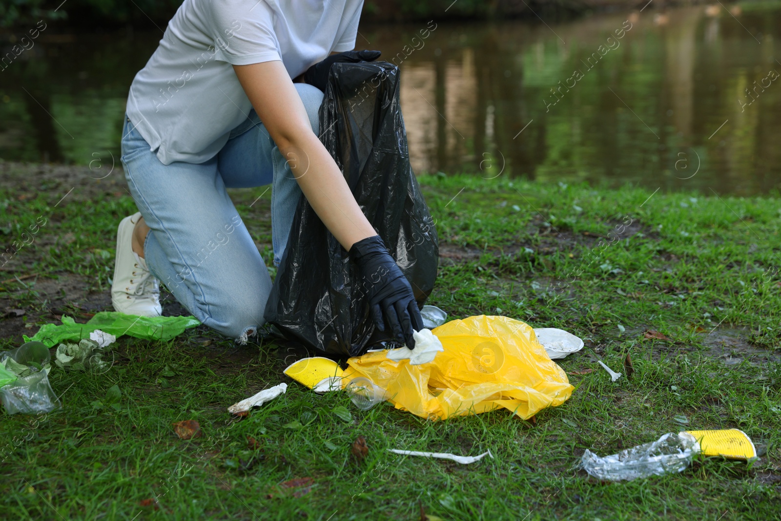 Photo of Woman with plastic bag collecting garbage in park, closeup