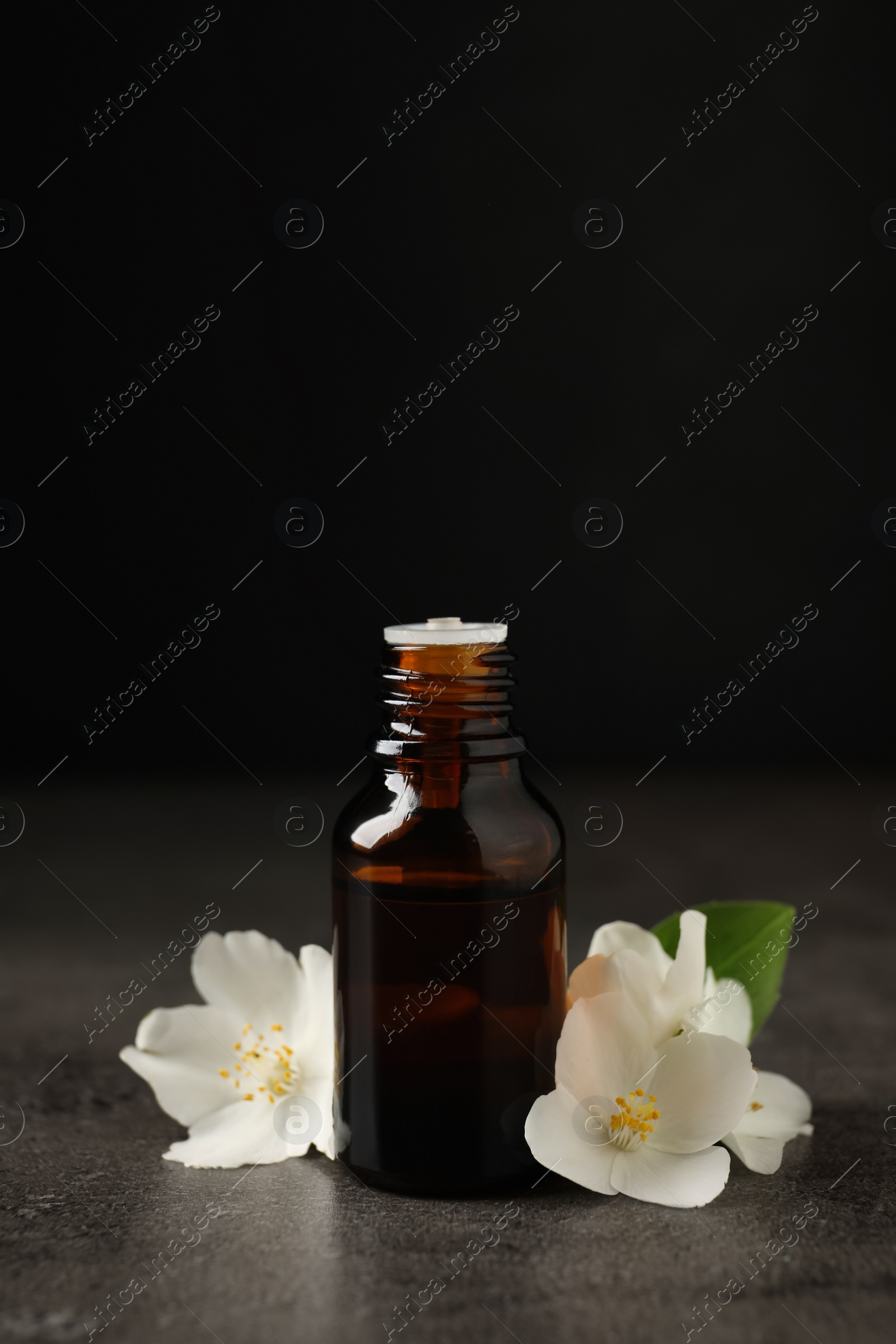 Photo of Essential oil and jasmine flowers on grey table