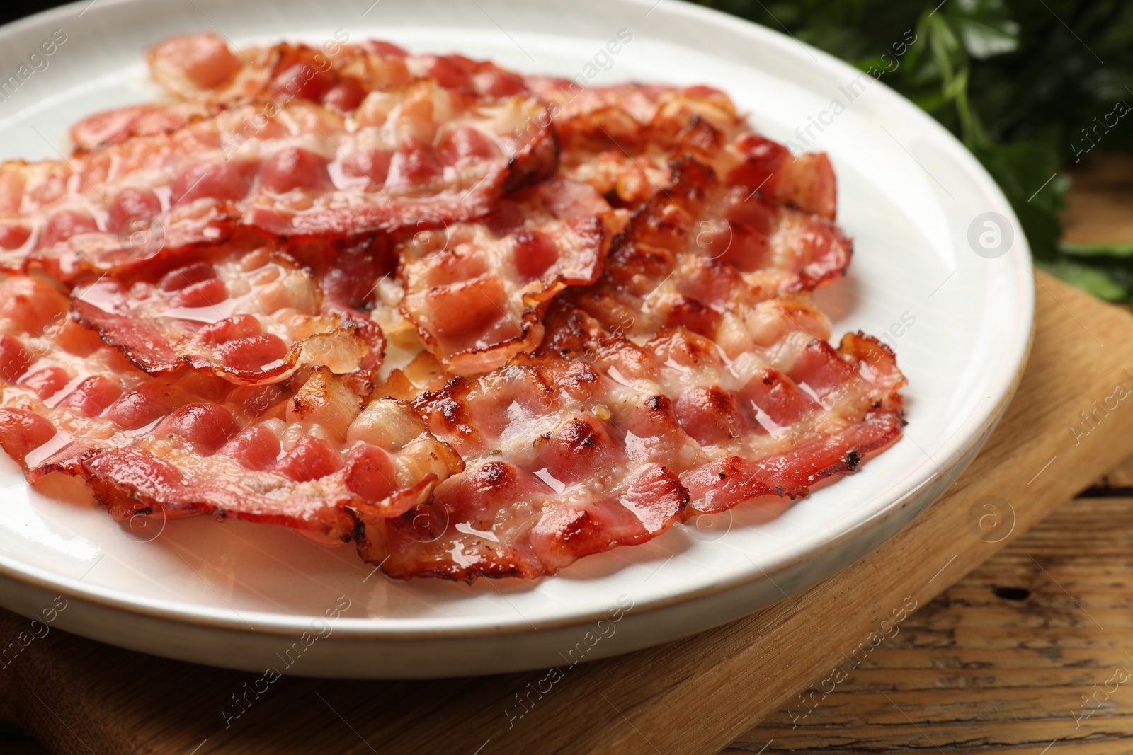 Photo of Plate with fried bacon slices on wooden table, closeup