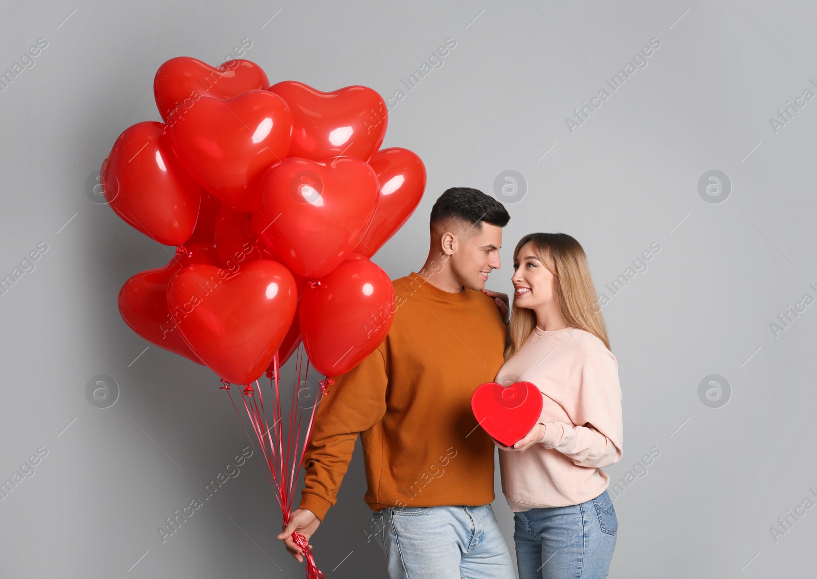 Photo of Lovely couple with heart shaped balloons and gift on grey background. Valentine's day celebration