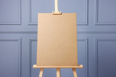 Wooden easel with blank board near grey wall indoors, closeup