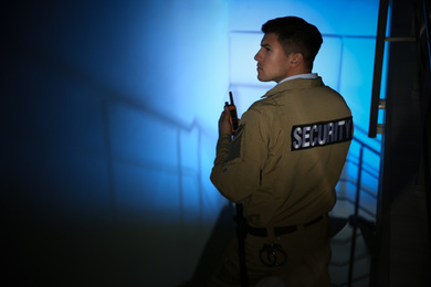 Professional security guard with portable radio set on stairs in dark room