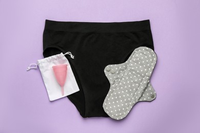 Photo of Women's underwear, reusable cloth pad and menstrual cup on violet background, top view