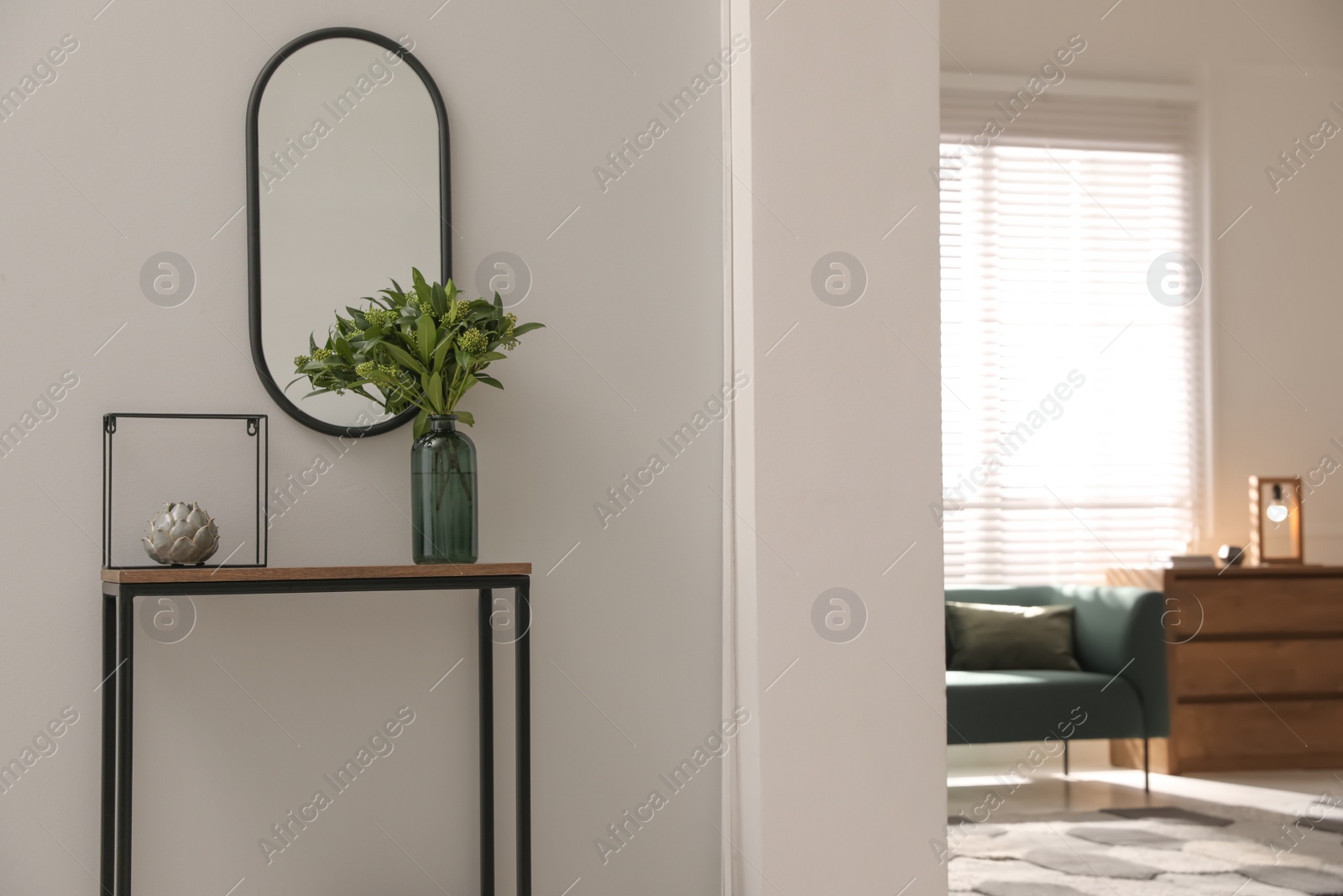 Photo of Console table with decor and mirror on light wall in hallway. Interior design