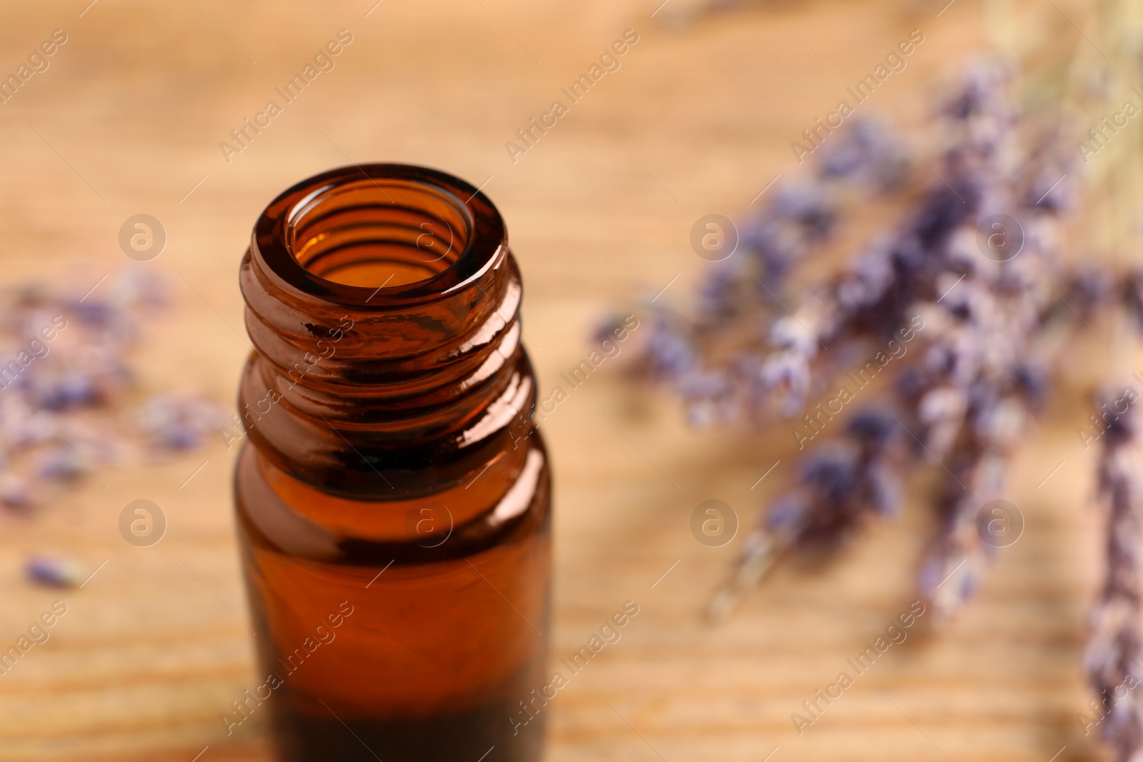 Photo of Bottle of essential oil and lavender flowers on wooden table, closeup. Space for text