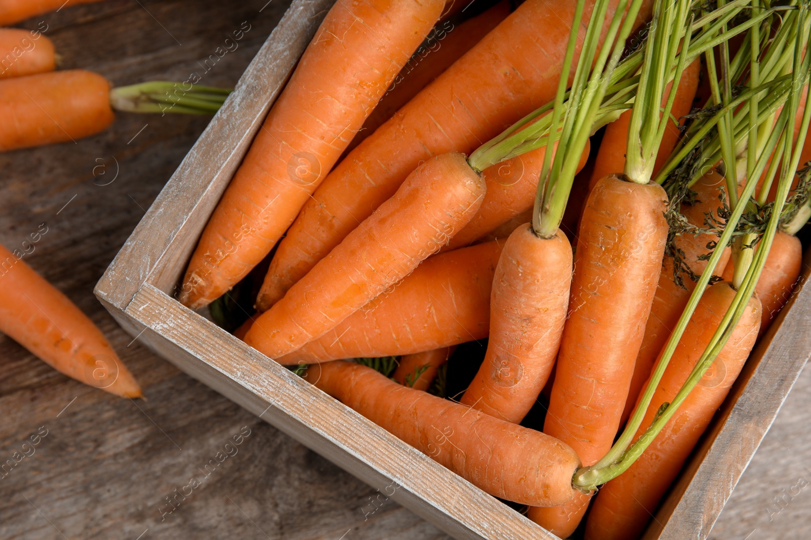 Photo of Crate with ripe carrots on wooden background, top view