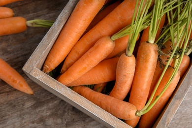 Crate with ripe carrots on wooden background, top view