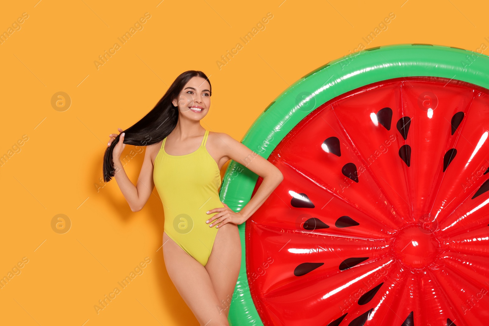 Photo of Young woman in stylish swimsuit near inflatable mattress against orange background