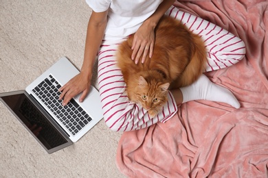 Woman with cute red cat and laptop on light carpet, top view