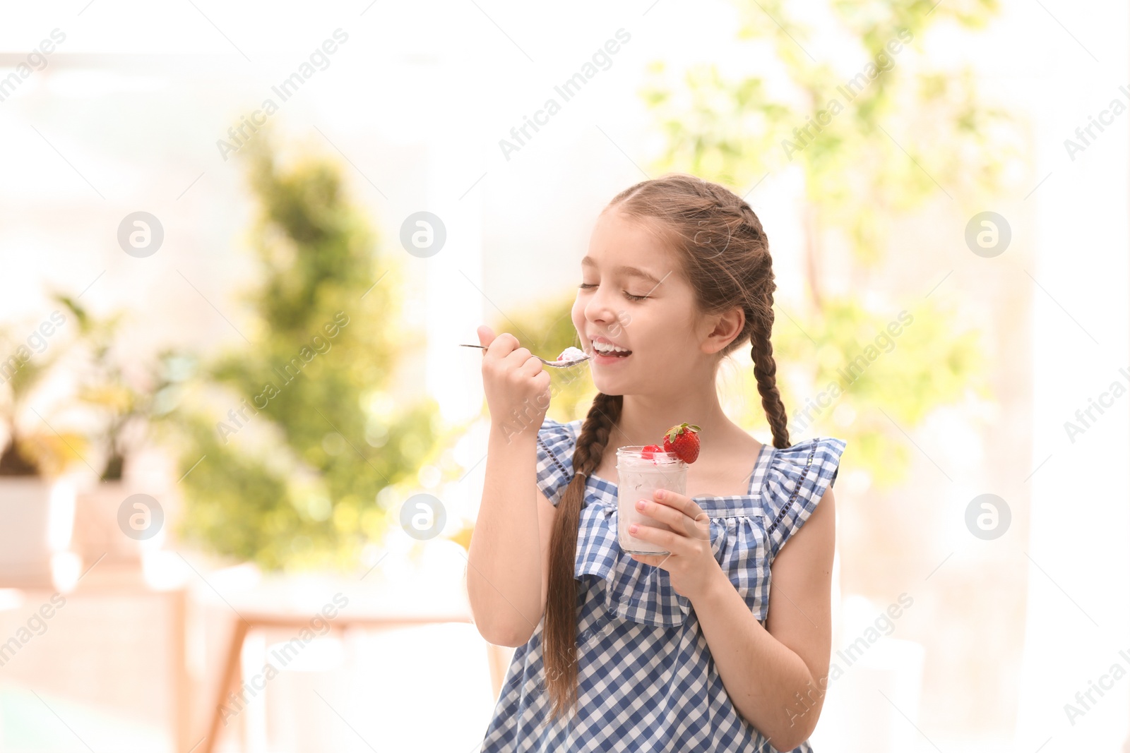 Photo of Cute girl eating tasty yogurt, indoors