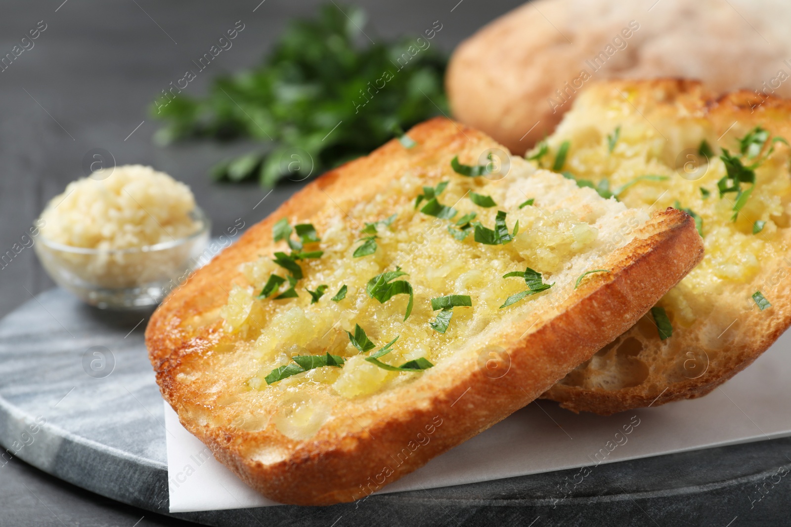 Photo of Slices of delicious toasted bread with garlic and herbs on grey table, closeup