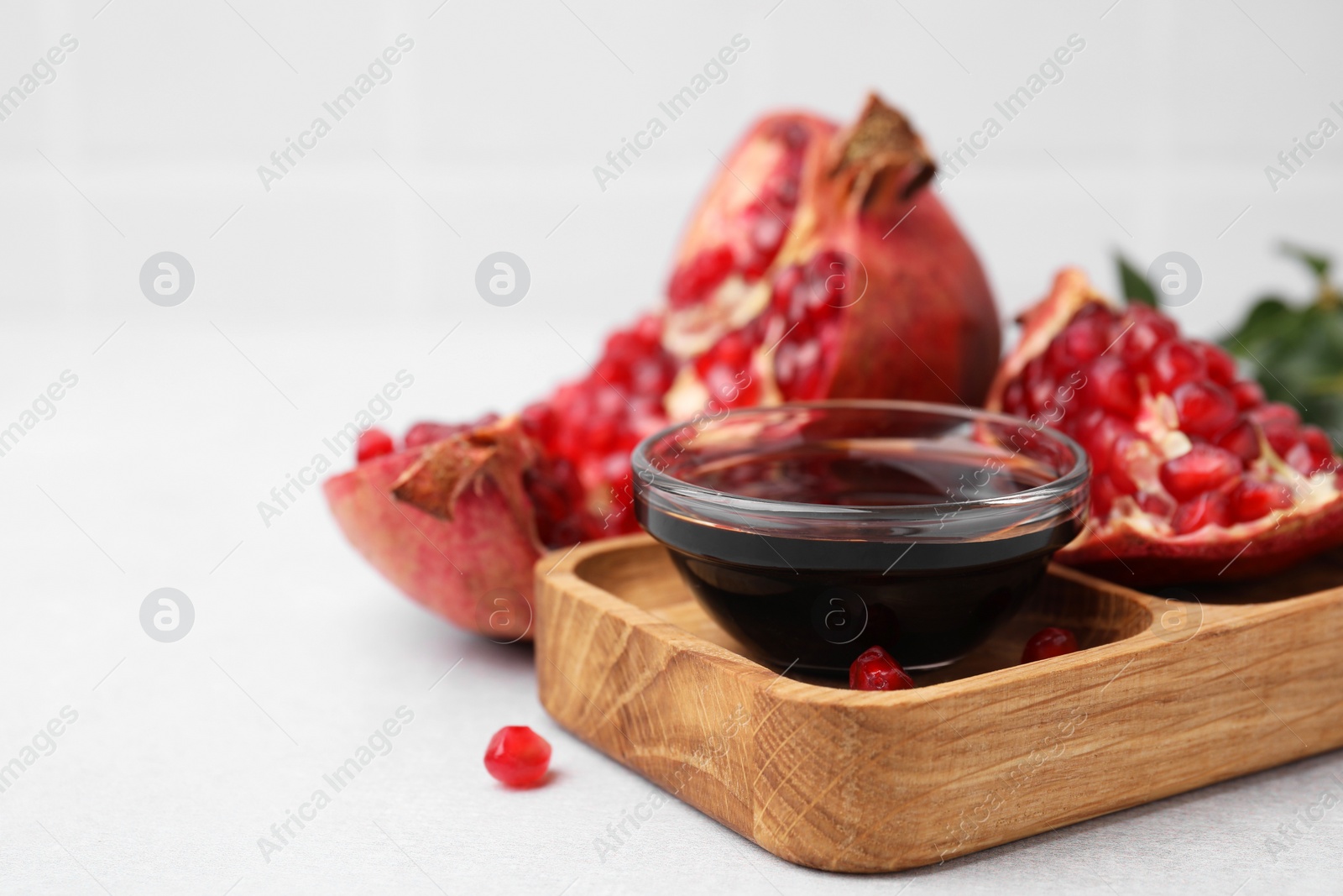 Photo of Tasty pomegranate sauce in bowl and fruits on light table, closeup. Space for text