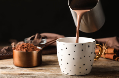 Pouring hot cocoa drink into cup on wooden table