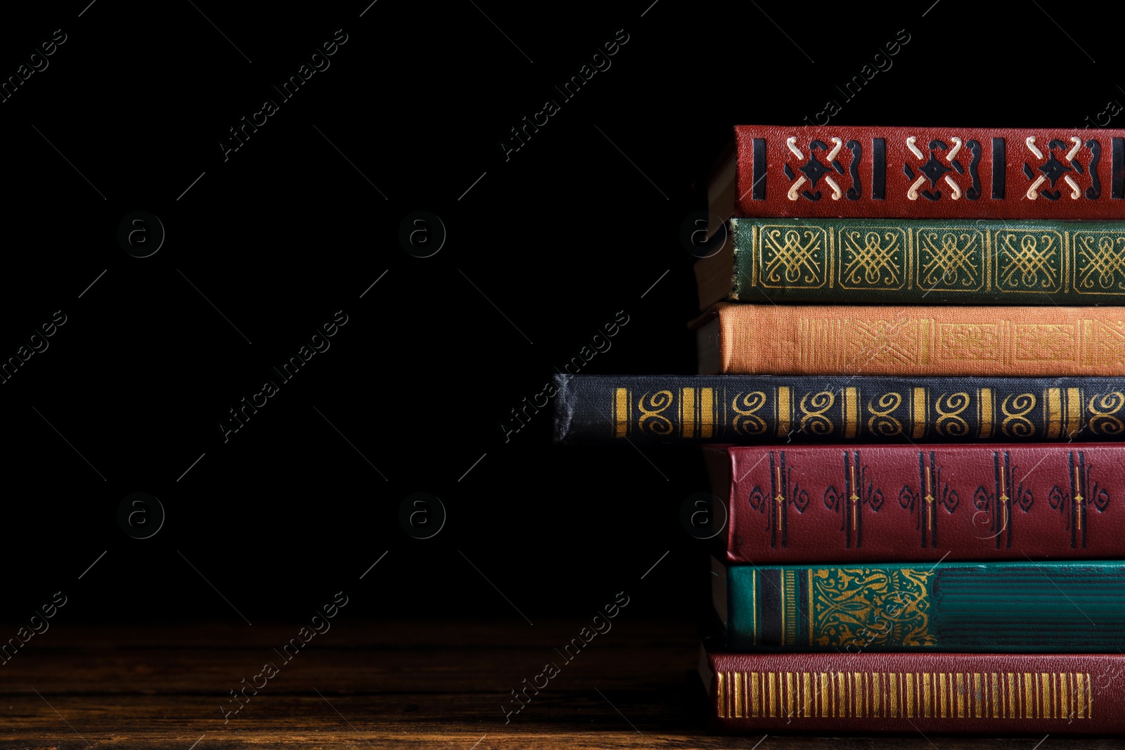 Photo of Collection of different books on wooden table against dark background. Space for text