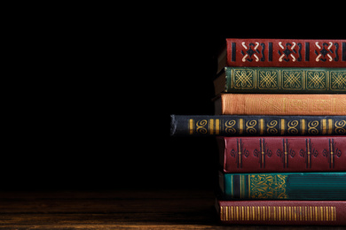 Photo of Collection of different books on wooden table against dark background. Space for text