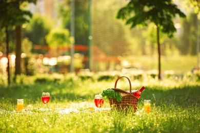 Photo of Picnic basket and glasses with drinks on green grass in park