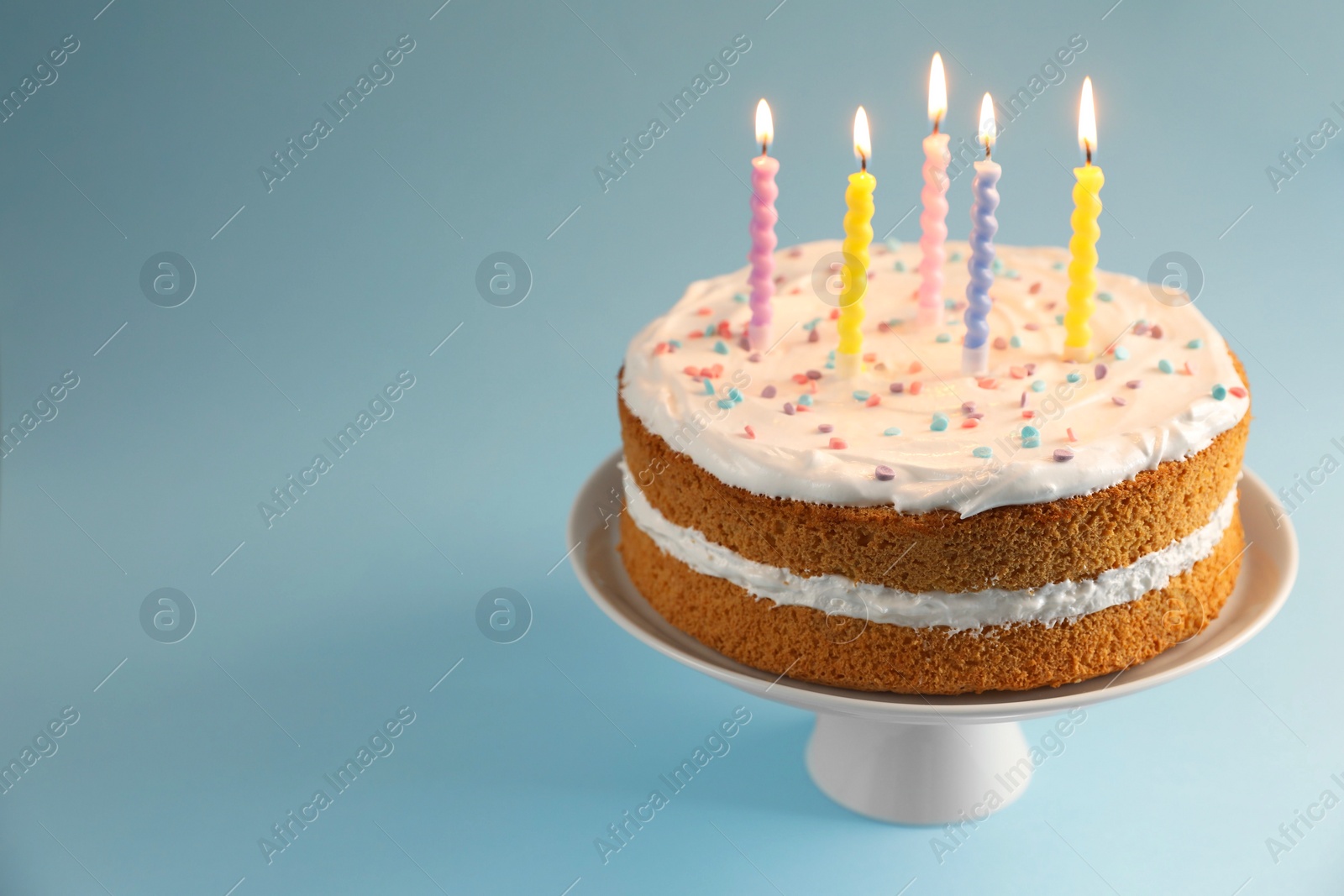 Photo of Tasty cake with colorful candles on light blue background, closeup. Space for text