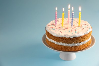 Photo of Tasty cake with colorful candles on light blue background, closeup. Space for text