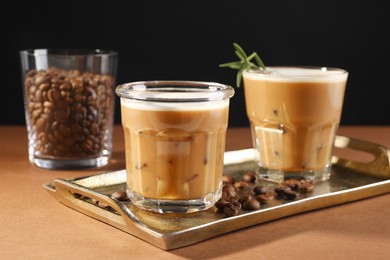 Refreshing iced coffee with milk in glasses and beans on brown table