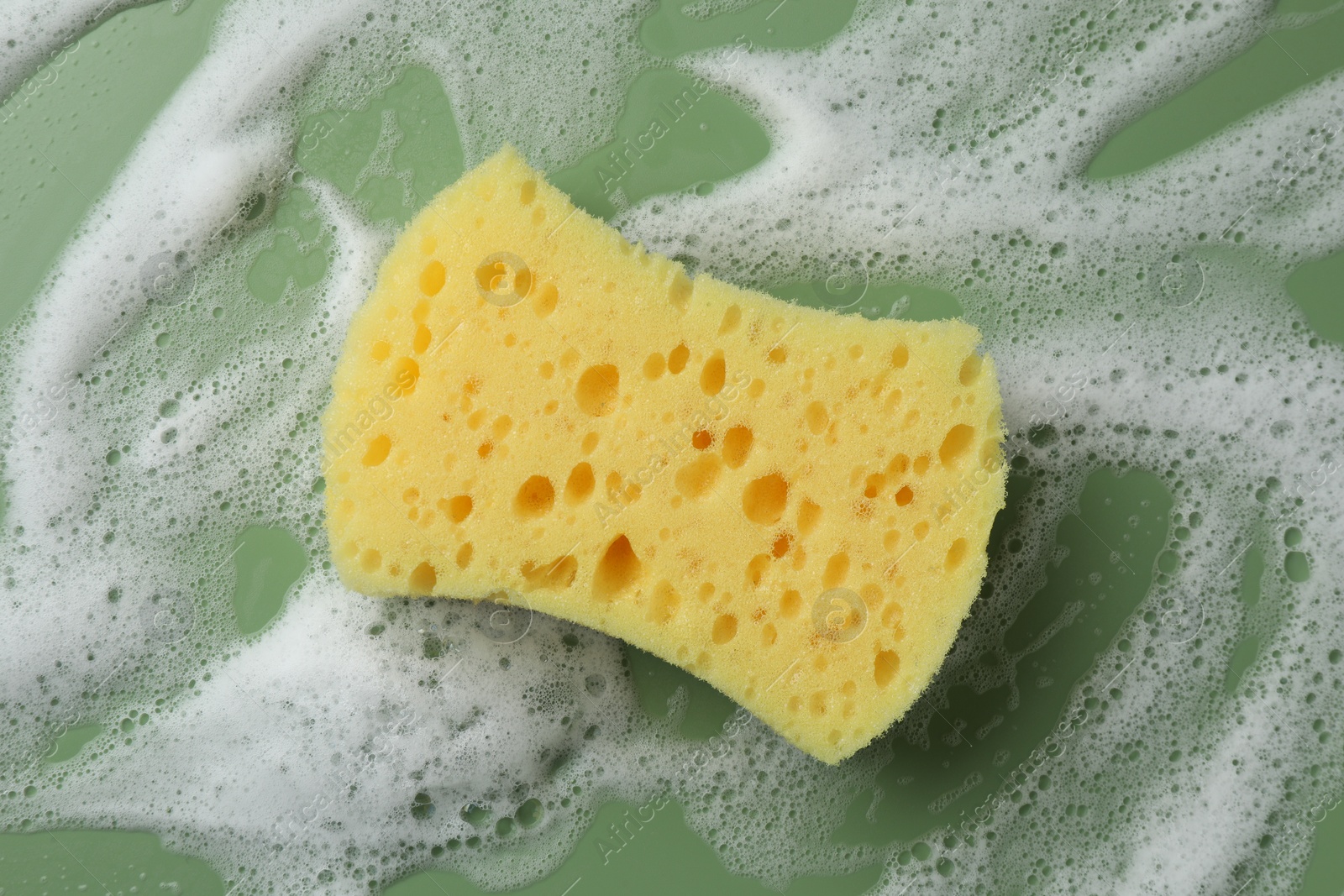 Photo of Yellow sponge with foam on green background, top view